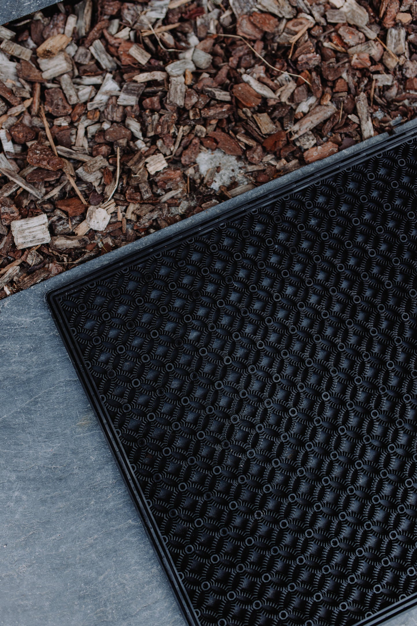 Close-up image of a black scraper mat, laying on a stone floor, highlighting the structure & modern design of the mat.