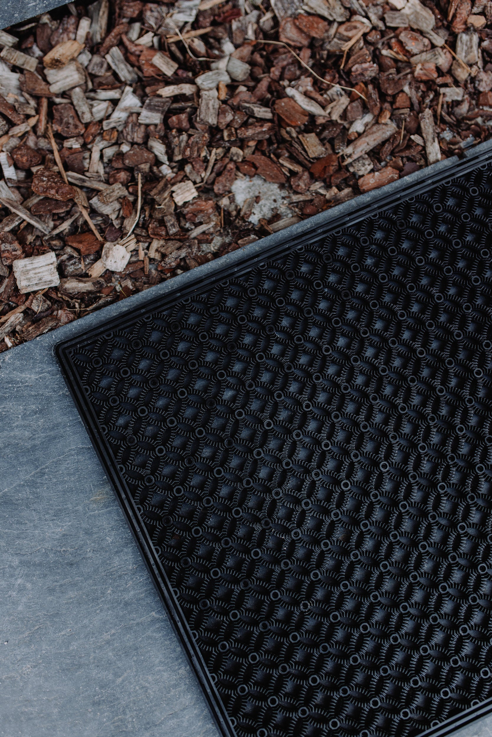 Close-up image of a black scraper mat, laying on a stone floor, highlighting the structure & modern design of the mat.