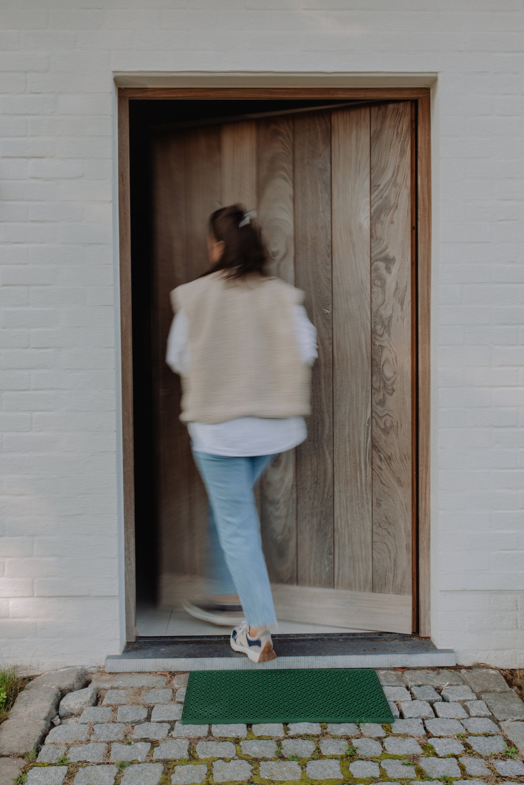 A woman enters her home, crossing over a green scraper mat.